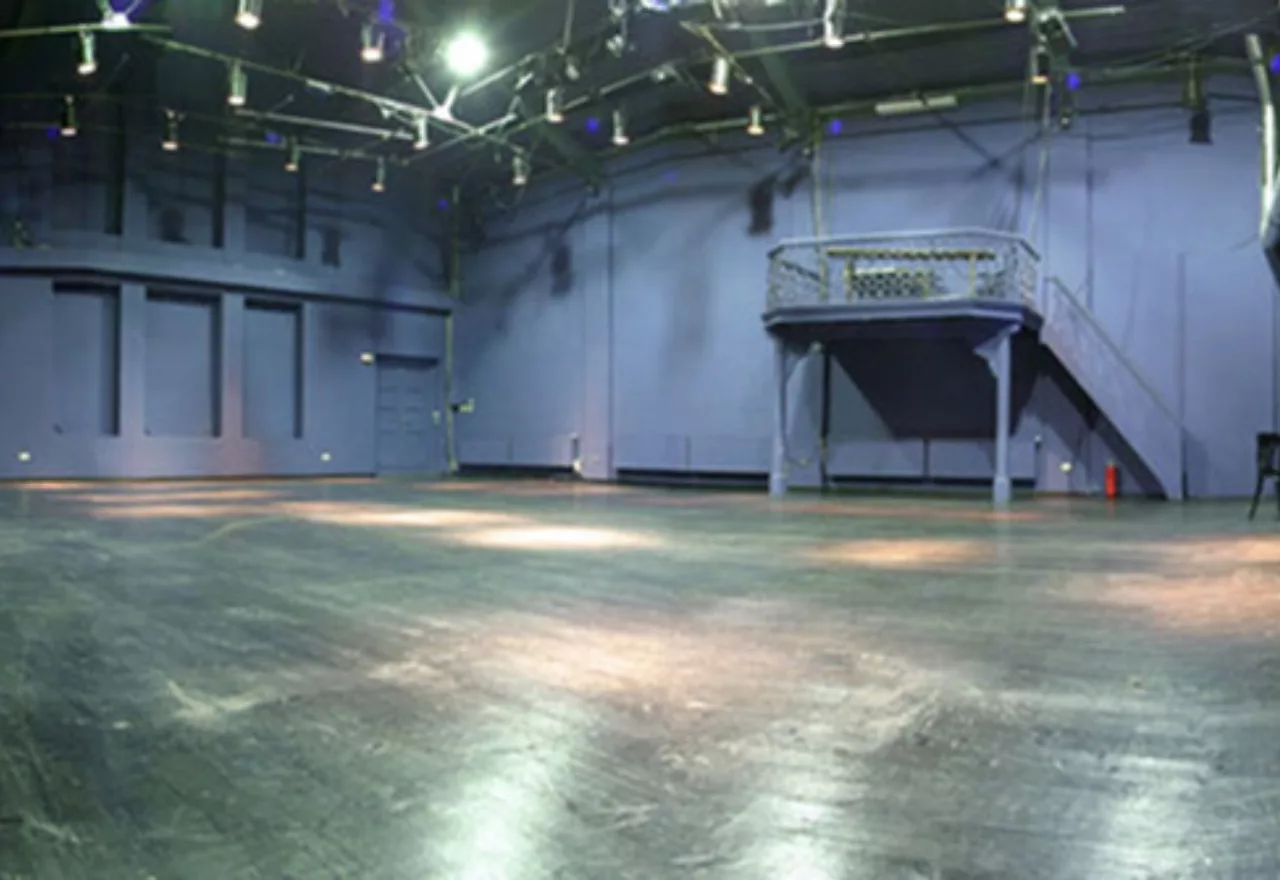 Das Bild zeigt den Bühnenraum im Theater im Ballsaal. Dort liegt schwarzer Tanzboden und die Wände sind hellgrau-blau gestrichen.